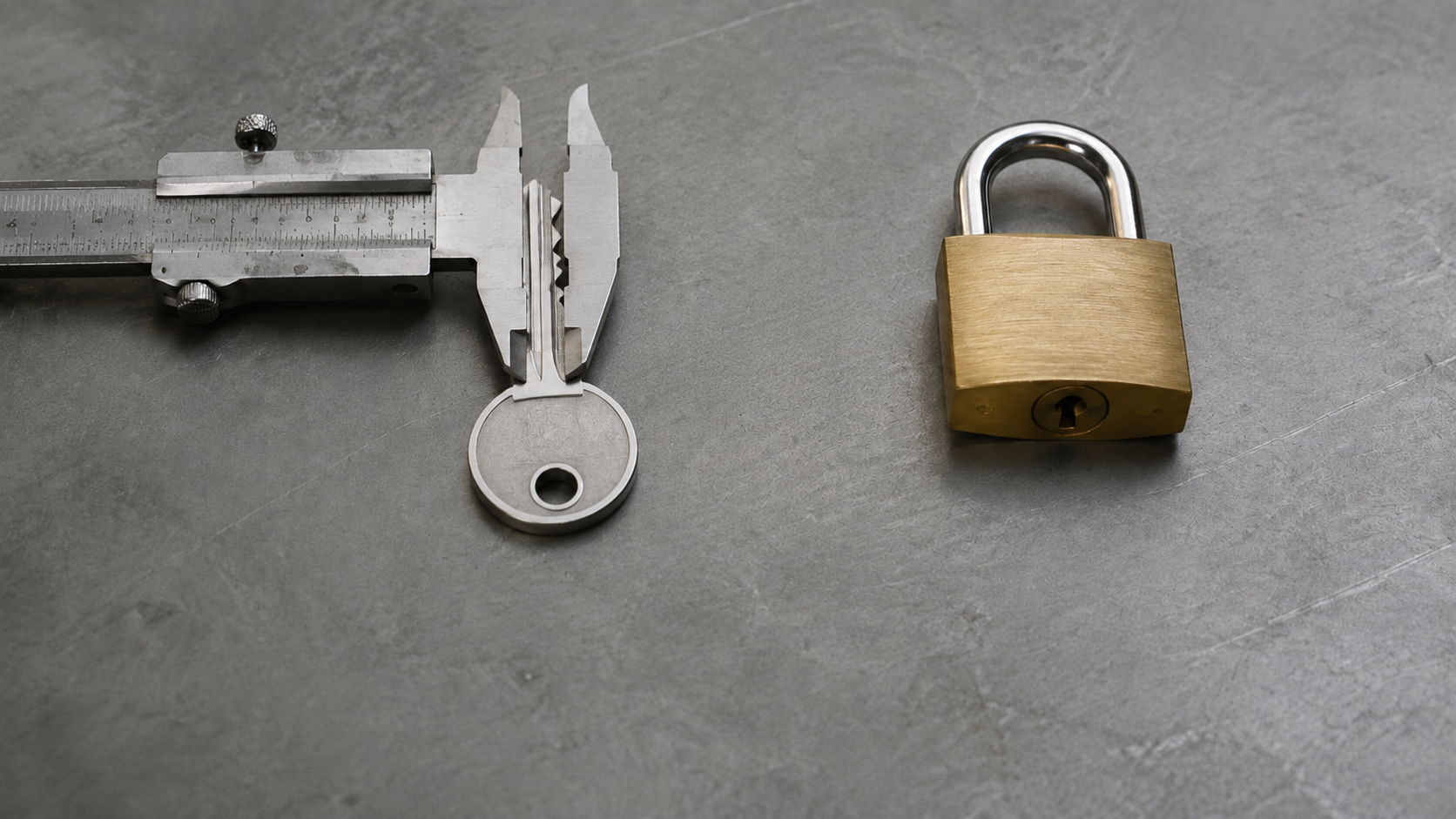 A caliper spans the width of a metal key beside a separate closed brass padlock.